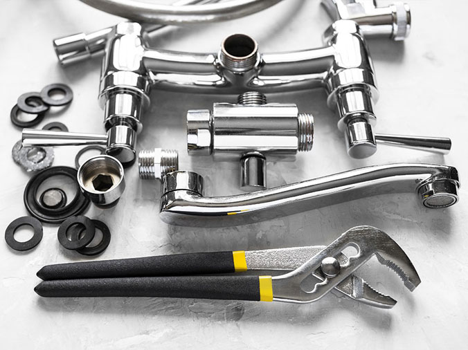 Disassembled chrome kitchen sink faucet with a plumbing wrench